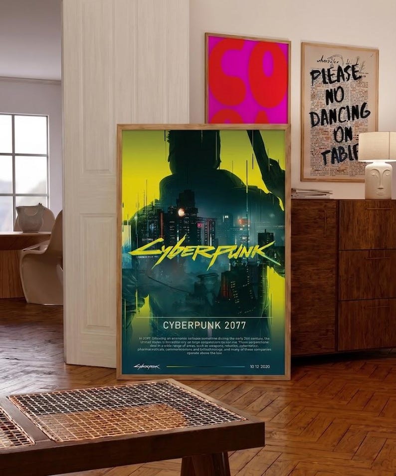 Op de afbeelding: Een ingelijste poster met de tekst "Cyberpunk 2077" in geel, met een silhouet en een stadsgezicht. De poster heeft een houten lijst en wordt op een houten vloer getoond. Andere ingelijste kunstwerken zijn zichtbaar op de achtergrond.