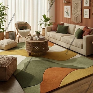 May include: A living room scene featuring a large area rug with an abstract design in shades of green, orange, and yellow. The room includes a beige sofa, a round wooden coffee table, and a woven chair. Decorative pillows and plants add to the cozy atmosphere.