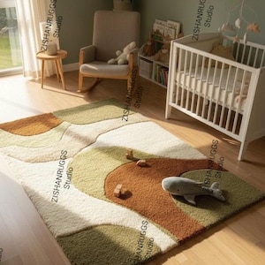 May include: A colorful area rug with a landscape design in shades of green, brown, and cream. A gray whale plush toy and wooden blocks are on the rug. The rug is in a nursery setting with a crib and rocking chair.