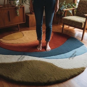 May include: A round rug with a wavy design in shades of orange, red, blue, white, and green. The rug is made of a soft, textured material and is placed on a wooden floor. The rug's design resembles a landscape.