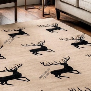 Könnte beinhalten: Beiger rechteckiger Teppich mit einem sich wiederholenden Muster aus schwarzen Hirschsilhouetten. Der Teppich besteht aus weichem Material. Das Design ist modern und für ein Wohn- oder Schlafzimmer geeignet. Maße in Zentimetern.