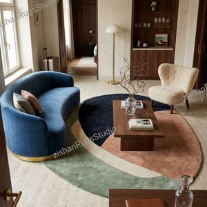 May include: A modern living room with a blue curved sofa, a patterned rug, and a wooden coffee table. The sofa has a gold base and is adorned with decorative pillows. A cream-colored armchair and a small side table are also present.