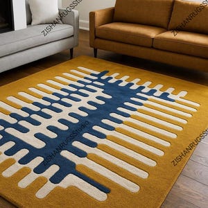 May include: Mustard yellow area rug with a geometric design in navy blue and white. The rug features a repeating pattern of connected lines and shapes, creating a modern aesthetic. The rug is placed on a hardwood floor, and the text "ZISHANRUGSStudio" is visible.