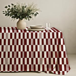 Könnte beinhalten: Eine bordeaux-weiß karierte Tischdecke mit einer Vase mit Grün, einer Schüssel, einem Teller und einem Glas. Die Tischdecke hat ein sich wiederholendes Muster aus bordeauxfarbenen Rechtecken und weißen Streifen. Die Vase ist beige, und die Schüssel und der Teller sind hellgrau.