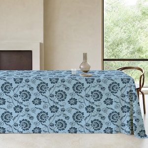 May include: A rectangular tablecloth featuring a light blue background with a repeating dark blue floral pattern of stylized blossoms, leaves, and swirling vines. The fabric drapes over a table surface, covering the top and sides completely.