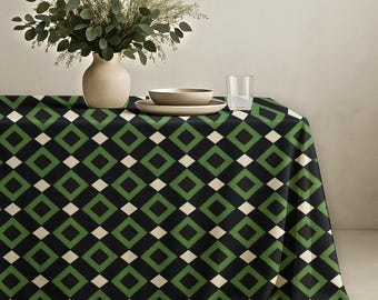 May include: A rectangular tablecloth featuring a repeating geometric pattern of black and green squares with small white diamond accents. The fabric drapes over a table surface, topped with a beige vase containing green foliage and a clear glass.