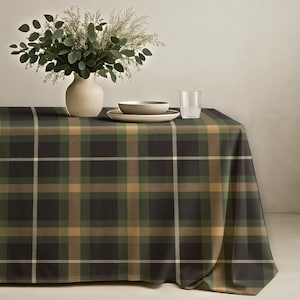 May include: A rectangular tablecloth featuring a plaid design in green, brown, and white hues. A vase with foliage, a bowl, a plate, and a glass of water are on the table. The tablecloth is draped over a table.