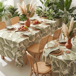 May include: A dining table set for a tropical-themed meal. The table is covered with a white tablecloth featuring a green leaf pattern. Woven chairs surround the table, and the setting includes plates, napkins, and decorative items.