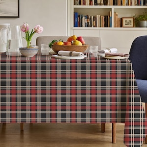 May include: A rectangular tablecloth featuring a dark charcoal, red, and beige plaid pattern. The fabric covers a dining table, displaying a symmetrical grid of intersecting lines that create a classic, multi-colored checkered design.