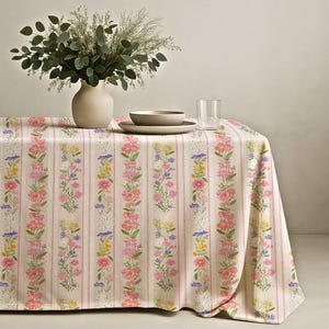 Puede incluir: Un mantel floral con rayas verticales y un patrón repetido de flores rosas, amarillas y azules. Un jarrón con vegetación, un cuenco, un plato y un vaso están sobre la mesa.