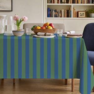 May include: A rectangular tablecloth featuring a repeating vertical stripe pattern in alternating shades of forest green and royal blue. The fabric drapes over the edges of a dining table, covering the surface completely with its bold, linear design.