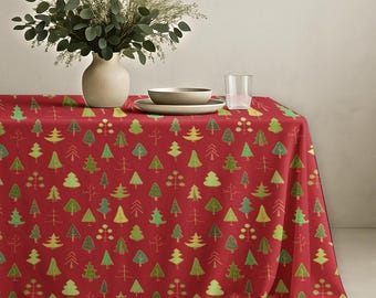 May include: A red tablecloth featuring a repeating pattern of stylized green and yellow evergreen trees. A beige ceramic vase filled with green eucalyptus branches, a beige ceramic bowl, and a clear glass tumbler sit on the table surface.