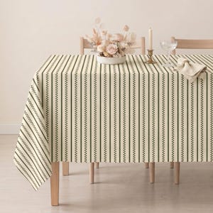 May include: A rectangular tablecloth featuring a pattern of vertical dark green stripes alternating with thin, checkered lines on a cream-colored background. The fabric drapes over the edges of a table, covering the surface completely in a uniform design.
