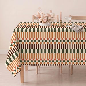 Könnte beinhalten: Eine rechteckige Tischdecke mit einem sich wiederholenden geometrischen Muster aus vertikalen Streifen und kleinen Quadraten in den Farben Dunkelgrün, gebranntes Orange und Creme. Der Stoff liegt auf einem Tisch und zeigt ein strukturiertes Design.