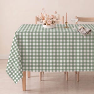 May include: A rectangular tablecloth featuring a sage green and white gingham check pattern. The fabric drapes over the edges of a table, displaying a consistent grid design across the entire surface, providing a clean and uniform appearance.