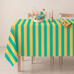 May include: A rectangular tablecloth featuring vertical stripes in alternating shades of bright yellow and teal. The fabric drapes over the edges of a table, creating a clean, geometric pattern that covers the entire surface of the dining furniture.