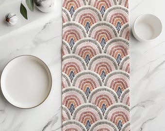 Puede incluir: Un camino de mesa rectangular con un patrón repetitivo en forma de abanico compuesto por pequeñas líneas discontinuas en tonos rosa empolvado, terracota y azul oscuro sobre un fondo crema, dispuesto en un diseño festoneado simétrico.