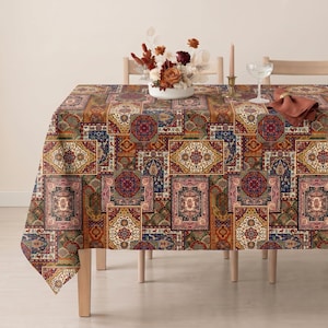 May include: A rectangular tablecloth featuring a patchwork design of intricate, multi-colored Persian-style rug patterns in shades of deep red, navy blue, gold, and cream. The fabric drapes over a table, displaying a repeating geometric motif.
