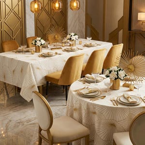 May include: Elegant dining room setting with two tables, one rectangular and one round, both covered with white tablecloths featuring a gold fan design. Gold chairs, place settings, and decorative accents complete the look. White flowers in gold vases add a touch of freshness.