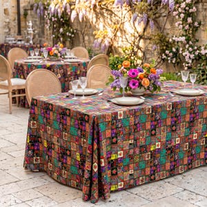 Puede incluir: Escena de comedor al aire libre con mesas cubiertas con un mantel colorido con estampado floral. Cada mesa está puesta con platos blancos, cubiertos y vasos transparentes. Un centro de mesa floral de flores rosas, naranjas y moradas.