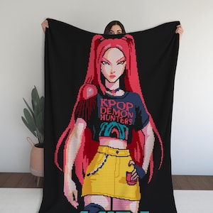 Puede incluir: Manta negra con una ilustración pixelada de una mujer con cabello rojo y falda amarilla. La mujer lleva una camiseta azul marino con el texto "KPOP DEMON HUNTERS". El nombre "MIRA" se muestra en azul en la parte inferior.