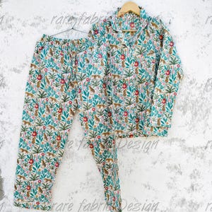 May include: A two-piece pajama set with a white background and a jungle-themed pattern. The pattern includes green leaves, red flowers, and brown leopards. The top has a collared neckline and long sleeves. The pants have a drawstring waist.