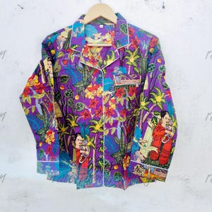 May include: A long-sleeved button-down shirt in a vibrant purple hue, featuring a colourful tropical jungle print with palm trees, flowers, and figures holding monkeys. The shirt includes a notched collar with white piping and a single chest pocket.