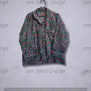 Può includere: Top pigiama con stampa floreale verde con bordini bianchi e chiusura con bottoni. Il top a maniche lunghe è appeso a una gruccia nera. Il tessuto presenta un motivo di fiori rosa e foglie verdi.
