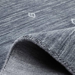 May include: A close-up of a blue rug with a diamond pattern. The rug has a textured surface and a rolled-up edge, revealing the underside. The diamond pattern is white and evenly spaced across the rug's surface. The rug appears to be made of a soft material.