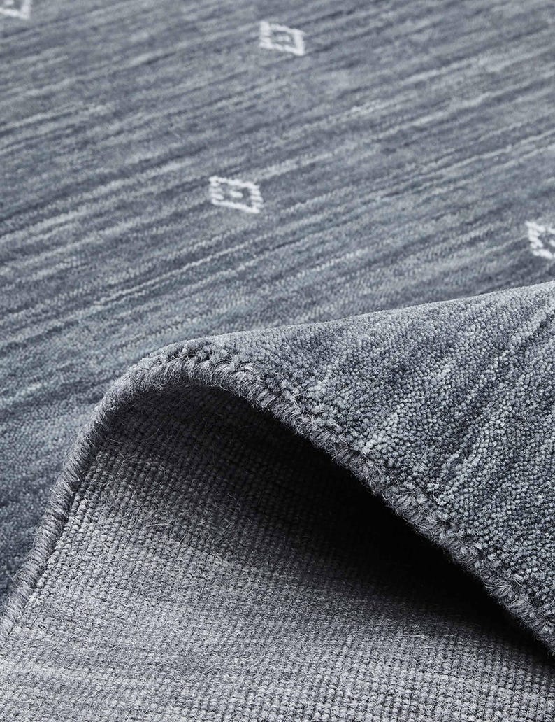 May include: A close-up of a blue rug with a diamond pattern. The rug has a textured surface and a rolled-up edge, revealing the underside. The diamond pattern is white and evenly spaced across the rug's surface. The rug appears to be made of a soft material.