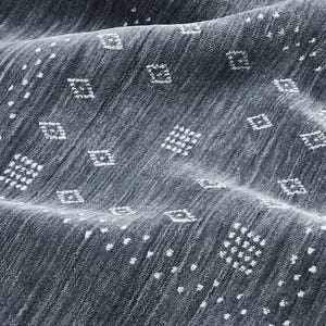 May include: Close-up of a textured, dark gray fabric with a subtle diagonal weave. The fabric is adorned with a repeating pattern of small white diamond shapes and scattered white dots, creating a visually interesting surface.