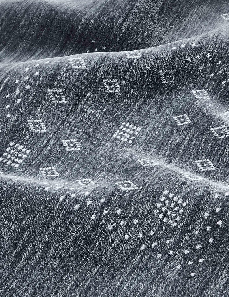 May include: Close-up of a textured, dark gray fabric with a subtle diagonal weave. The fabric is adorned with a repeating pattern of small white diamond shapes and scattered white dots, creating a visually interesting surface.
