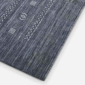 May include: A rectangular, dark blue rug with a textured surface. The rug features white geometric patterns and dotted lines. The design is a mix of stripes and repeating shapes, creating a modern aesthetic.