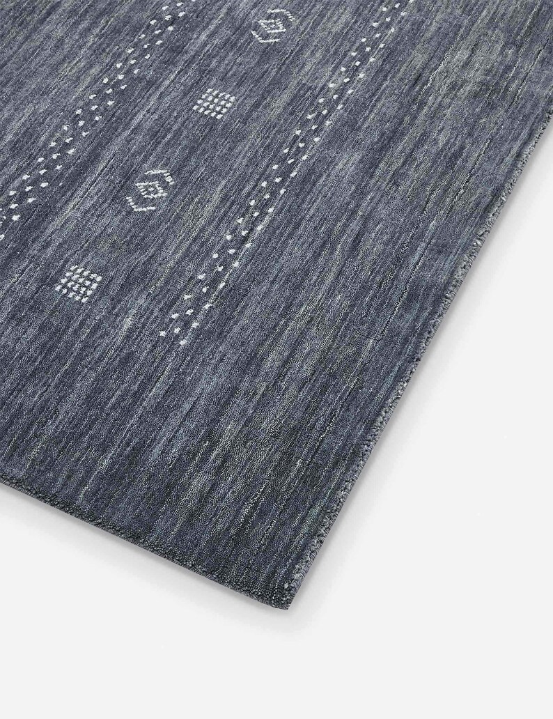 May include: A rectangular, dark blue rug with a textured surface. The rug features white geometric patterns and dotted lines. The design is a mix of stripes and repeating shapes, creating a modern aesthetic.