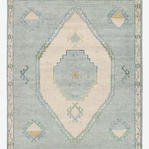 Könnte beinhalten: Rechteckiger Teppich mit hellblauem Grund und einem zentralen Rautenmuster in Creme und Hellblau. Er weist geometrische Muster in Grün, Blau und Gold auf, mit einem Fransenrand. Ideal für Wohn- und Schlafzimmer, ca. 200 cm x 150 cm.