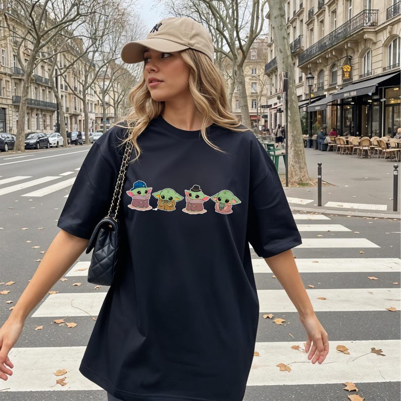 Pu&ograve; includere: Una t-shirt nera a maniche corte con una stampa grafica di quattro piccoli personaggi alieni verdi in vari abiti, inclusi cappelli e sciarpe, abbinata a una borsa a tracolla trapuntata nera e un berretto da baseball beige con un logo scuro.