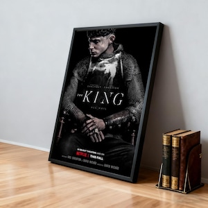 Könnte beinhalten: Ein gerahmtes Filmplakat für "The King" mit einer sitzenden Figur in Rüstung. Das Poster hat einen schwarzen Rahmen und lehnt an einer Wand. Der Titel und die Namen der Schauspieler sind sichtbar. Ein Buchstützen mit Büchern befindet sich im Vordergrund.