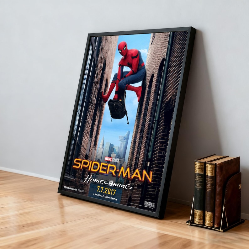 May include: Framed movie poster for Spider-Man: Homecoming. The poster features Spider-Man in a red and blue suit, hanging between brick buildings. The title is in gold lettering, with the release date 7.7.2017.