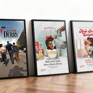 Puede incluir: Tres carteles enmarcados con bordes negros se apoyan contra una pared. Los carteles presentan anuncios de estilo vintage de "Corn Flakes" y "Main Street Delights", y un cartel de película de "Welcome to Derry."