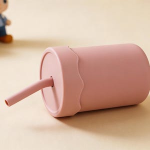 May include: A pink sippy cup with a matching straw. The cup has a wavy design around the lid. Two small figurines are in the background.