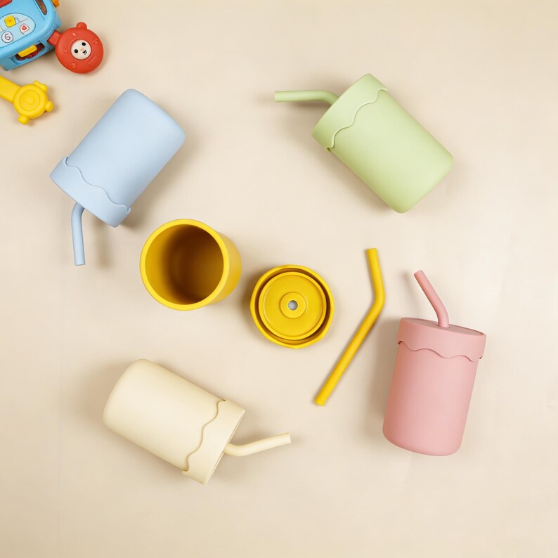 May include: A collection of colorful silicone cups with straws, in pastel shades of blue, green, pink, and yellow. One cup is disassembled, showing the lid and cup separately. The cups have a wavy design around the rim.