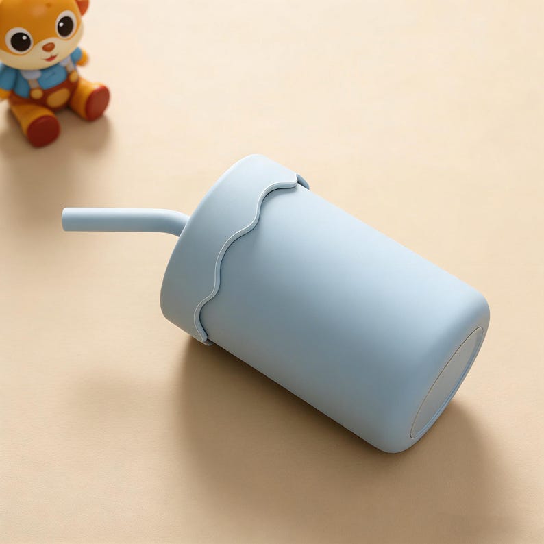 May include: A light blue tumbler with a matching lid and straw. The lid has a wavy edge design. A small toy bear is visible in the background.