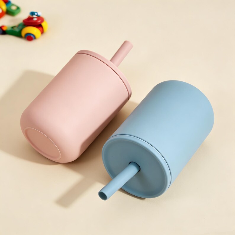 Puede incluir: Dos vasos de colores pastel con pajitas. Uno es rosa claro, el otro azul claro. Ambos tienen un dise&ntilde;o simple y moderno. Los vasos probablemente est&aacute;n hechos de un material suave y mate.