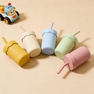 May include: Five colorful silicone cups with straws in yellow, cream, blue, green, and pink. Each cup has a wavy rim and a matching straw. A toy car is in the upper left corner.