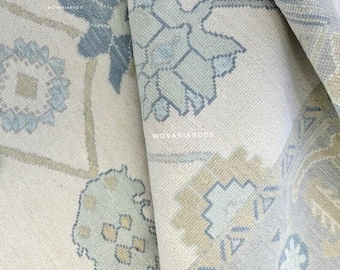 May include: Close-up of a rolled-up rug with a floral pattern. The rug features a cream-colored background with blue, light blue, and tan floral designs. The rug's texture is visible, and the design is intricate.