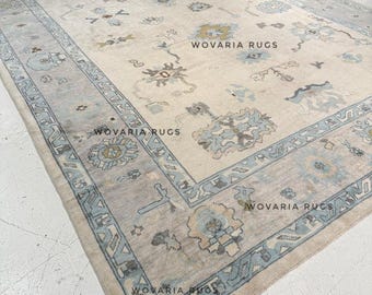 May include: Large rectangular rug with a cream-colored field and a light blue border. The rug features floral and geometric patterns in shades of blue, beige, and gray. The text "WOVARIA RUGS" is visible on the rug.