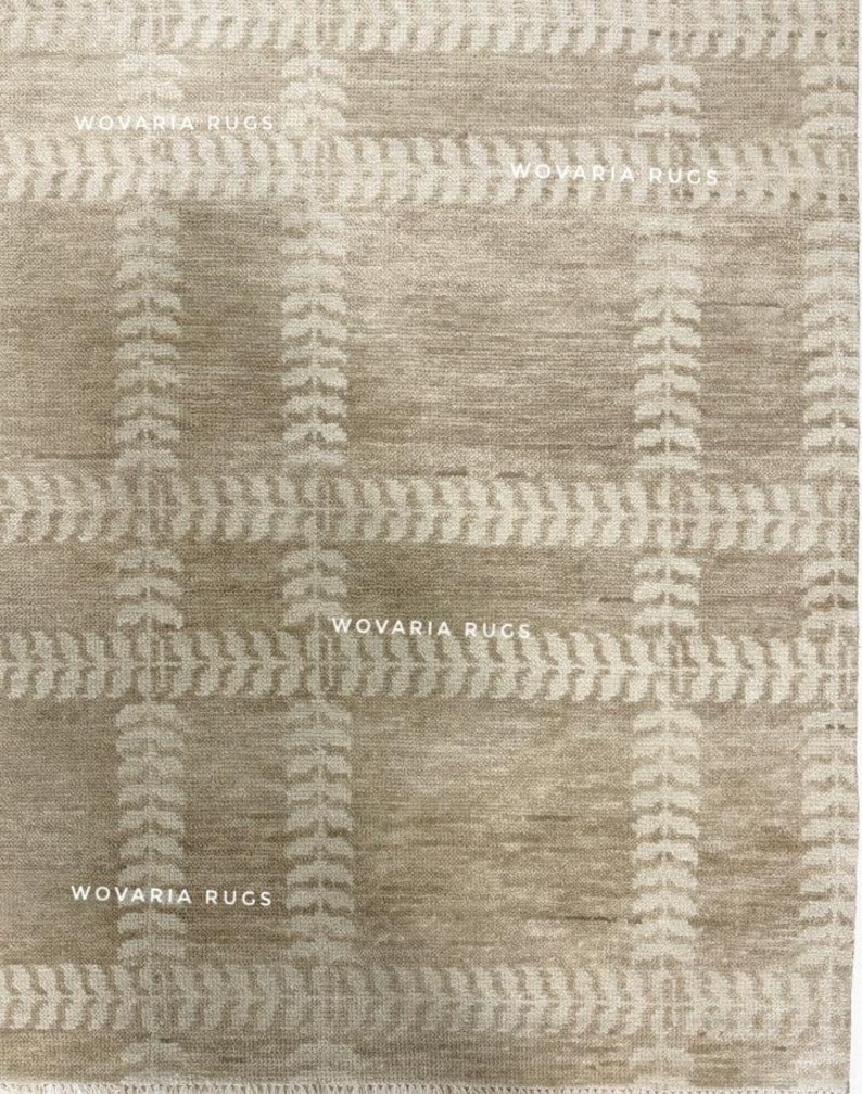 May include: Beige area rug with a plaid pattern. The rug features a grid design with vertical and horizontal lines, and leaf-like patterns. The text "WOVARIA RUGS" is printed in white across the top and bottom of the rug.