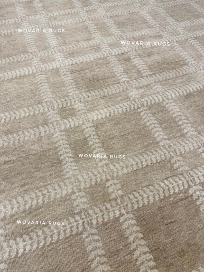 May include: Beige area rug featuring a repeating grid pattern. The grid is formed by white, leaf-like designs. The rug has a textured appearance and the text "WOVARIA RUGS" is visible in multiple places.
