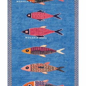 Könnte beinhalten: Ein rechteckiger blauer Teppich mit einem sich wiederholenden Muster aus bunten Fischen. Jeder Fisch hat ein anderes Design, mit orange, rosa, schwarzen und lila Farbtönen. Der Teppich hat einen gemusterten Rand und den Text "WOVARIA RUGS".