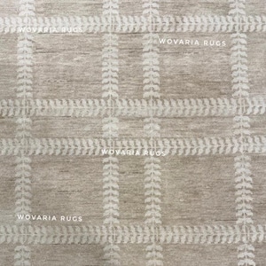 May include: A beige rug with a grid pattern. The design incorporates vertical and horizontal lines with a repeating leaf-like motif in a lighter shade. The text "WOVARIA RUGS" is printed across the image.
